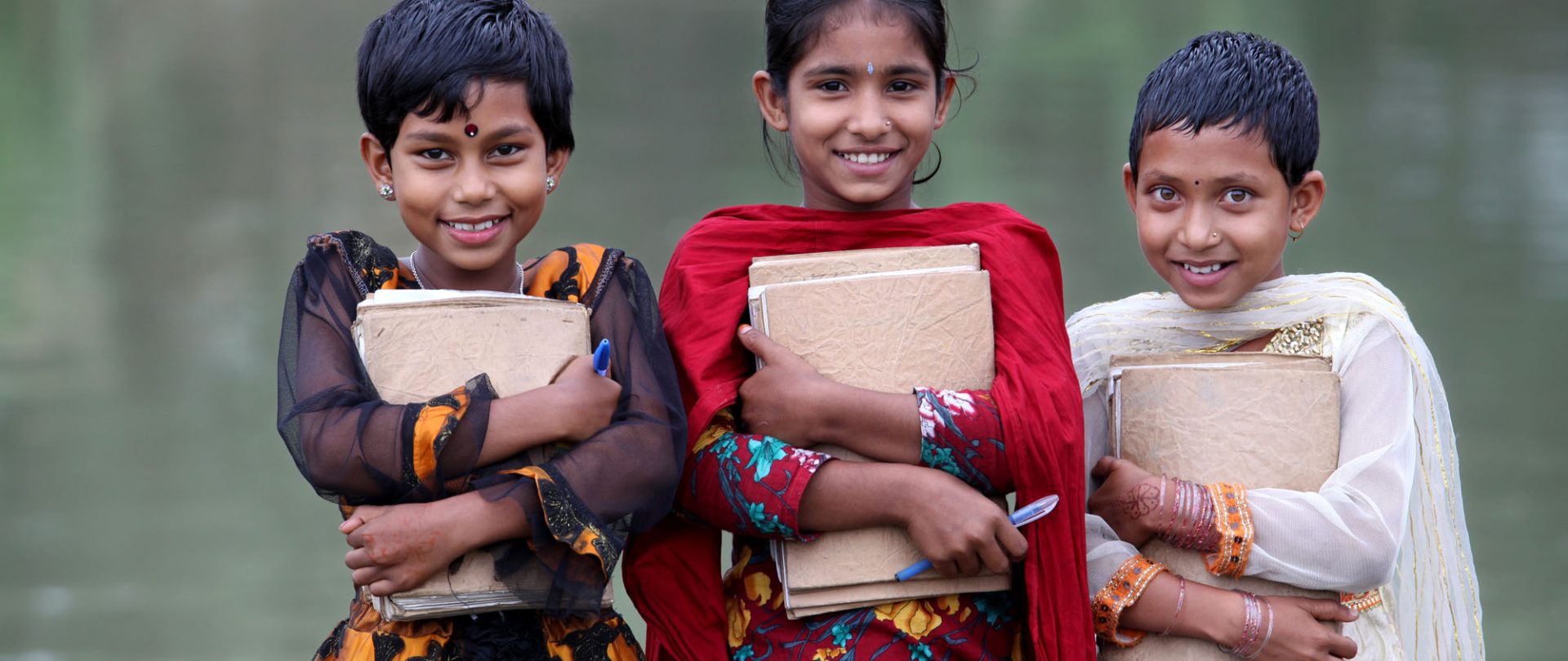 Three girls smile while standing in front of the open deck holding their books at the boat school, Shanto Nagar, Singara, Natore. 03 November 2012. Photo: Abir Abdullah/SSS
